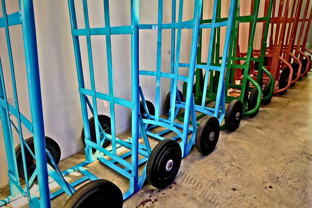 แถวรถเข็น 2 ล้อ โครงเหล็กหลากสีสัน ทั้งสีฟ้า สีเขียว และสีส้ม วางเรียงรายพร้อมใช้งานในคลังสินค้า